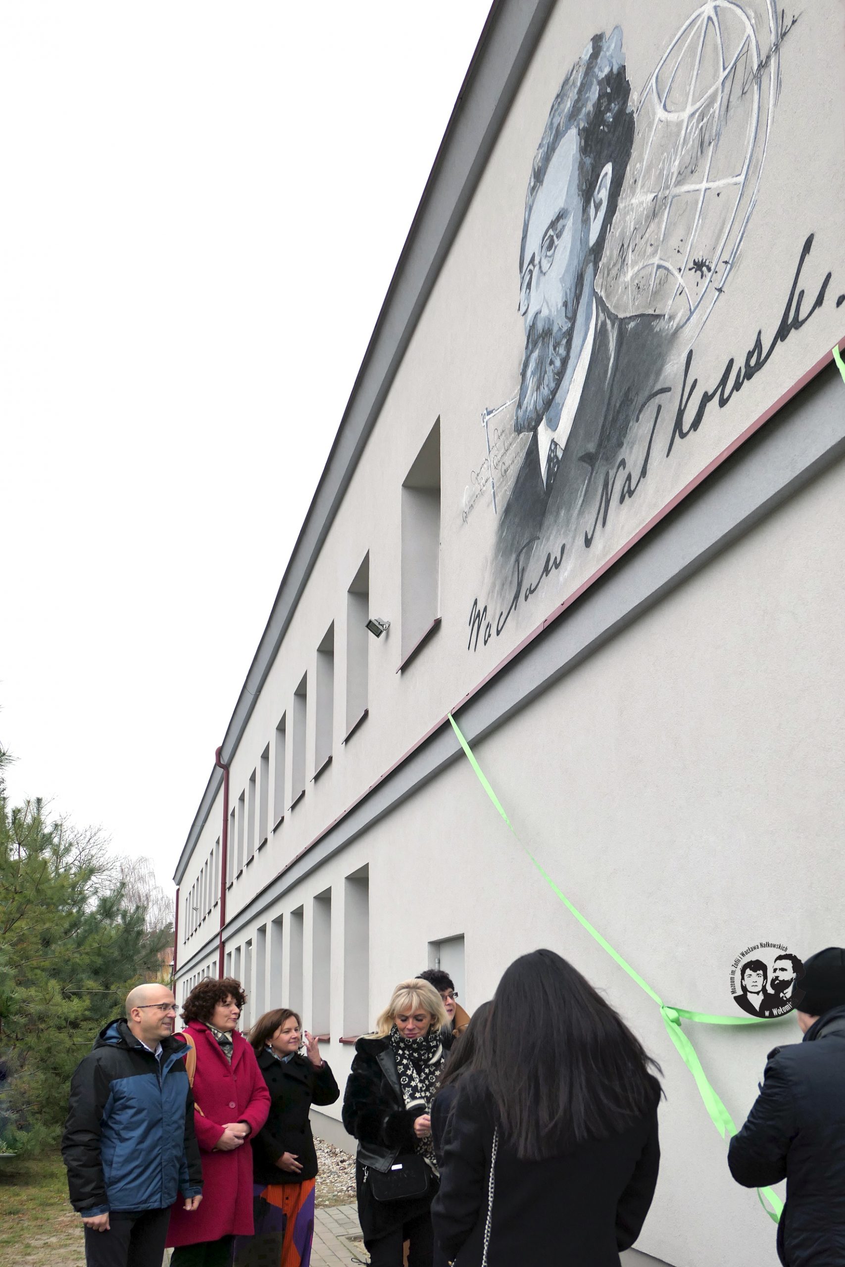 Fotografia kolorowa, pionowa, wykonana w momencie odsłaniania muralu, czyli przecinania zielonej wstęgi