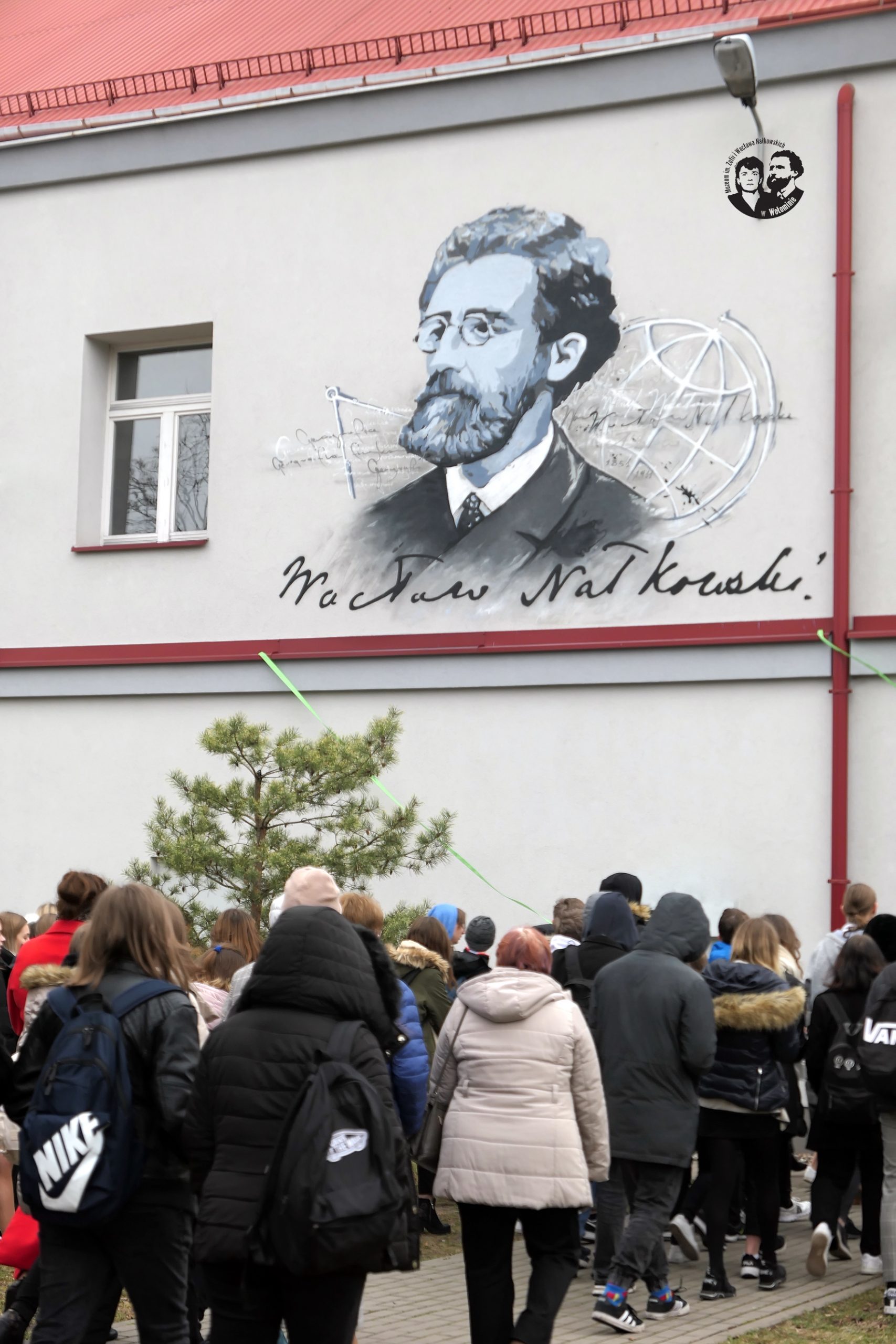 fotografia kolorowa, pionowa, w dolnej części zdjęcia widać tyłem młodzież, w górnej fragment ściany budynku z muralem