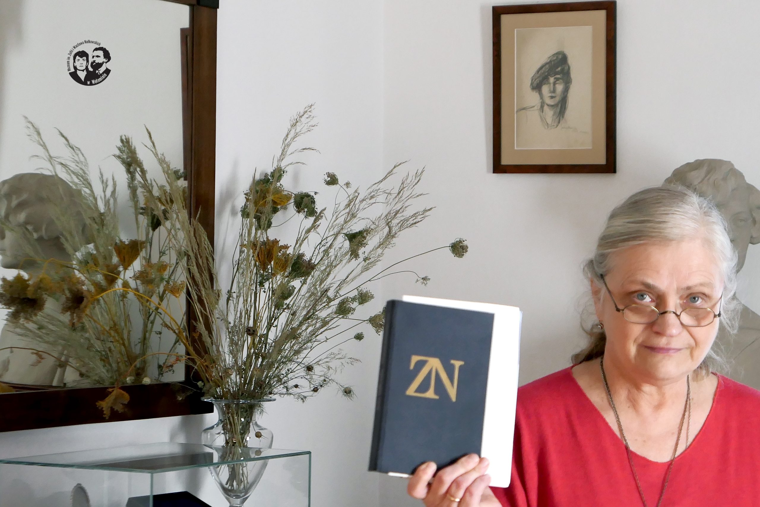 Fotografia kolorowa, sytuacyjna, na zdjęciu prof. dr hab. Maria Jolanta Olszewska trzymająca w ręku książkę ze zbiorem dramatów Zofii Nałkowskiej