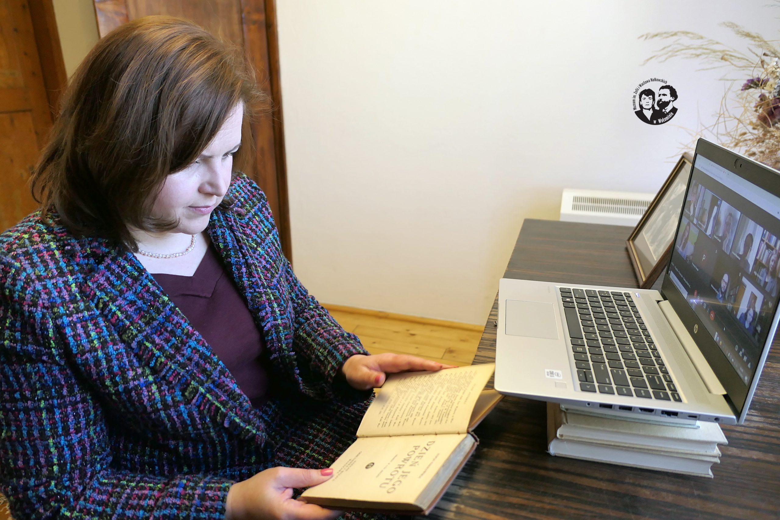 Fotografia kolorowa, sytuacyjna, wykonana w bibliotece muzeum, na zdjęciu widoczny monitor komputera z osobami biorącymi udział w panelu oraz  Agata Sobczak z książką „Dzień jego powrotu”
