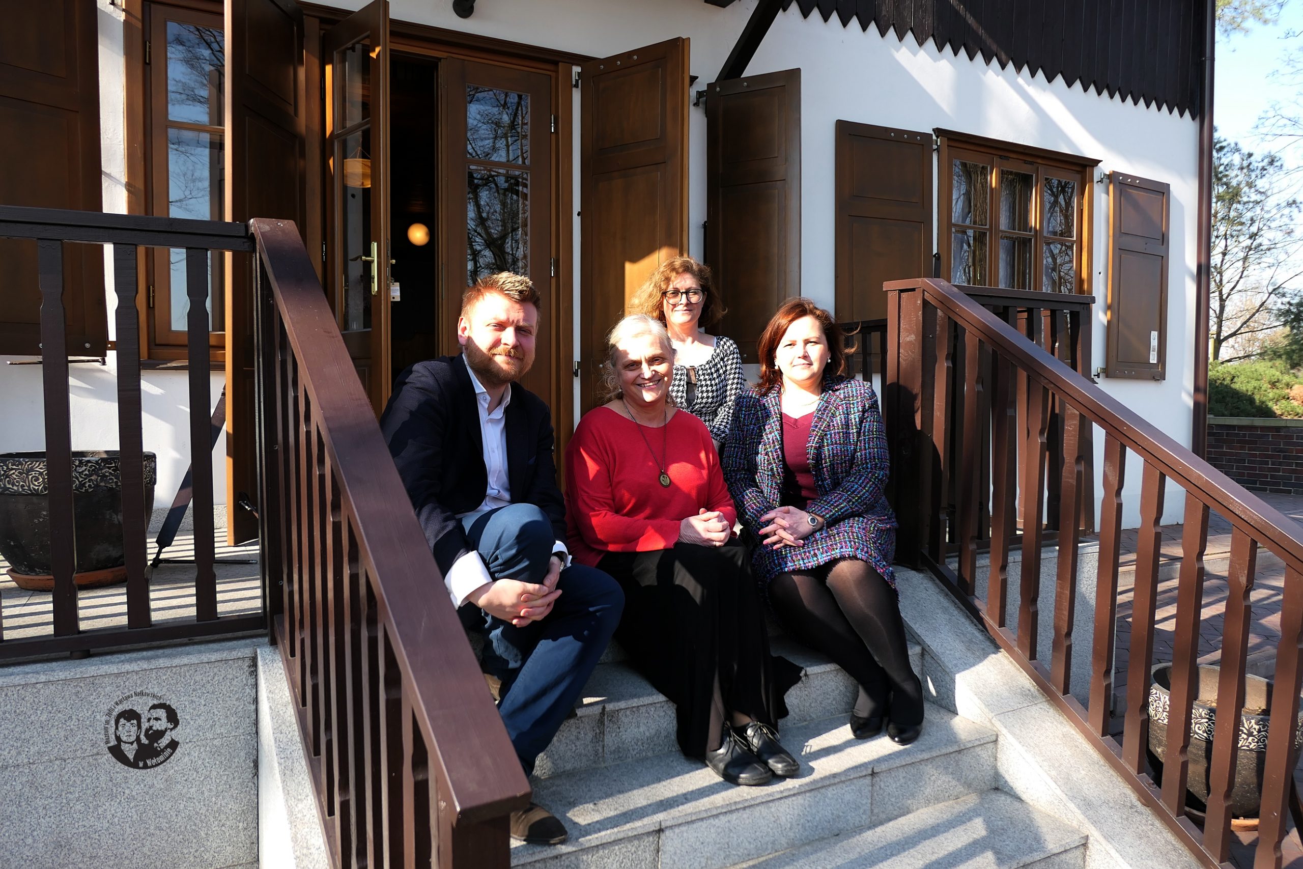 Fotografia kolorowa, sytuacyjna, na schodach przed budynkiem muzeum od strony południowej, na zdjęciu siedzą od lewej dr hab. Karol Samsel, prof. dr hab. Maria Jolanta Olszewska, Krystyna Gostyńska oraz Agata Sobczak